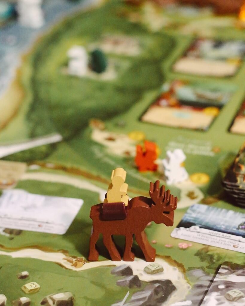 Close-up of the Everdell board with a brown wooden moose figure carrying a pale worker meeple across a green forest landscape dotted with resource tokens and cards.
