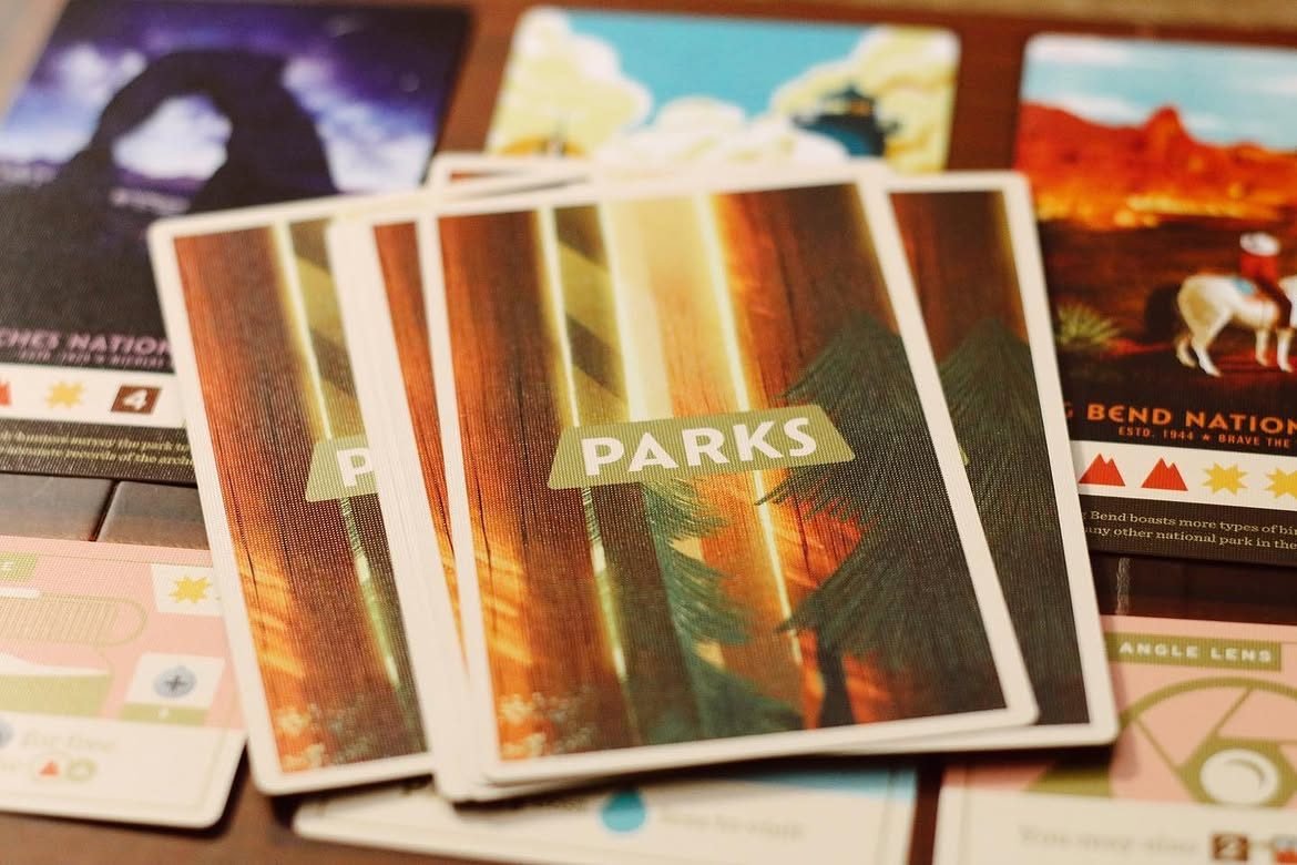 A stack of Parks cards showing the sequoia-forest 'PARKS' card back, surrounded by national-park cards with vintage-poster illustrations.