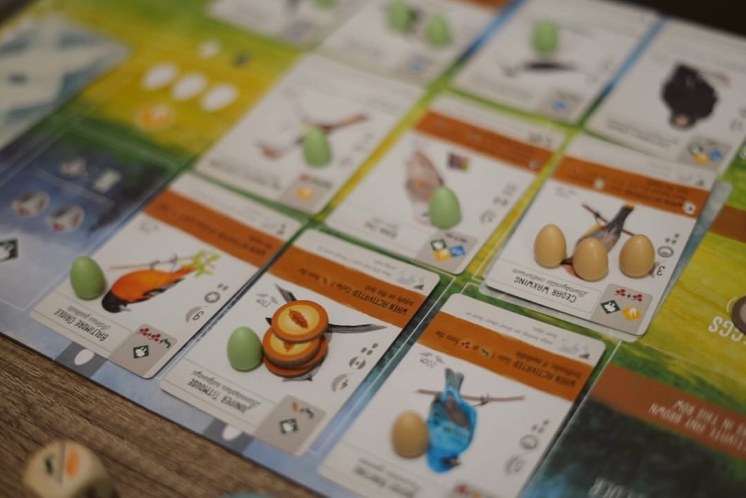 Rows of Wingspan bird cards with pastel eggs placed on them, seen at a low angle across the player mat.